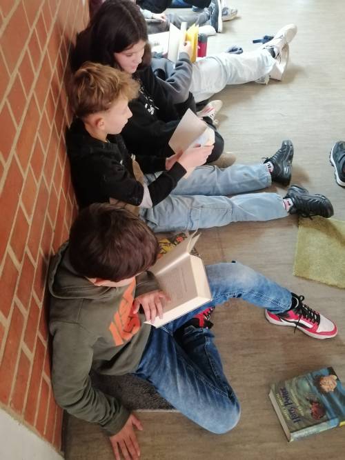 Schüler sitzen mit Büchern auf Teppichfliesen und lesen für sich selbst oder vor.